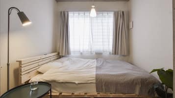 Un lit simple avec une tête de lit en bois, une table de chevet avec un verre et un luminaire suspendu.