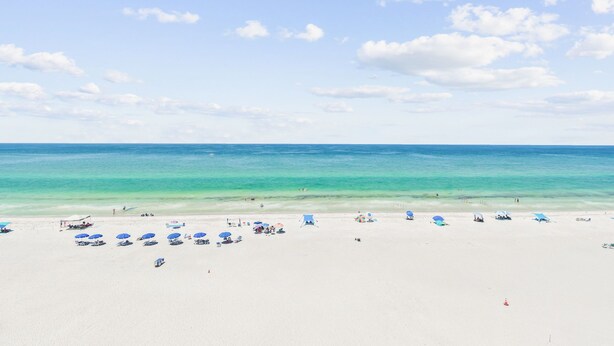 A beach with clear turquoise water, white sand, and scattered umbrellas.