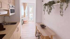 Una cocina moderna con armarios de madera, microondas integrado y un lavamanos. Hay un pequeño comedor con una mesa y bancos.