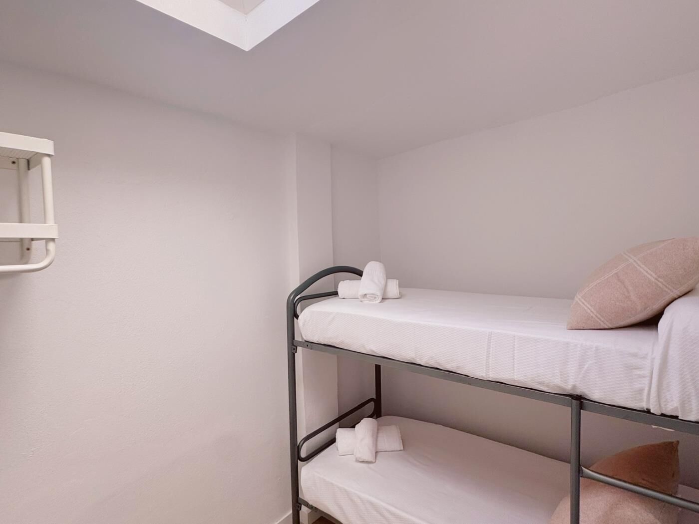 Une chambre avec un lit superposé, une lucarne, une petite étagère blanche et un seul oreiller marron.