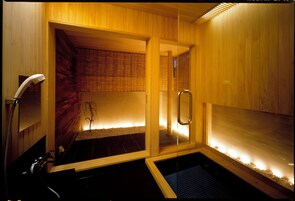 A sauna with wooden walls and a glass door, a bench, and a small pool.