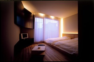A hotel room with a bed, a bedside table with a lamp, a TV on a stand, and a window with curtains.