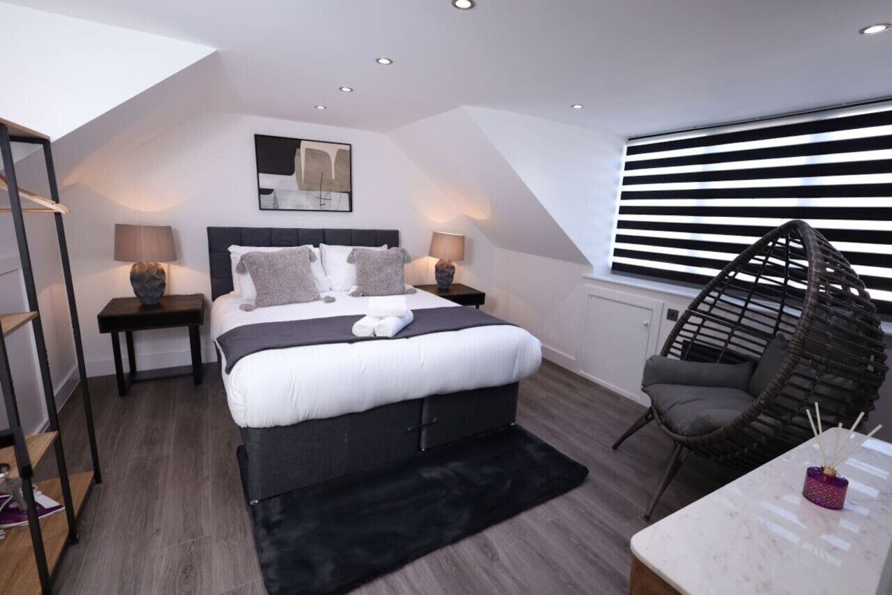 A modern bedroom with a large bed, two bedside tables, a hanging chair, and a window with blinds.