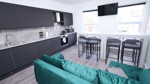 A modern kitchen with dark cabinets, a large window, and a green sofa. - Market Street 61A (Watford)