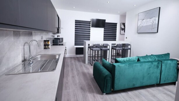 A modern kitchen with a sink, a dining area with a table and chairs, and a green sofa. - Market Street 61A (Watford)
