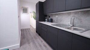 A modern kitchen with dark cabinets, a stainless steel sink, and a countertop. - Market Street 61A (Watford)