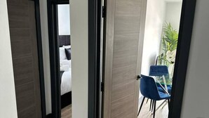 A modern hotel room with a wooden floor, a bed with white linens, a blue chair, and a small plant on a table. - Modern Newly Renovated flat - Elstree & Borehamwood Railway Station (Hertfordshire)