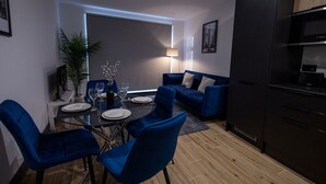 A modern living room with a dining area, featuring blue furniture, a black cabinet, and a Bosch oven. - Modern Newly Renovated flat - Elstree & Borehamwood Railway Station (Hertfordshire)