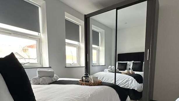 A modern hotel room with a large bed, a wardrobe, and a view of the city. - Modern Newly Renovated flat - Elstree & Borehamwood Railway Station (Hertfordshire)