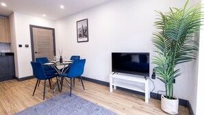 A modern living room with a dining table, blue chairs, a flat-screen TV, a large potted plant, and a framed picture on the wall. - Modern Newly Renovated flat - Elstree & Borehamwood Railway Station (Hertfordshire)