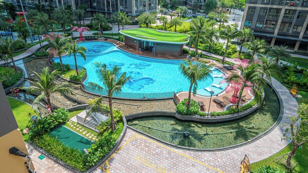 Una piscina grande de varios niveles con palmeras y zonas de descanso alrededor, rodeada de edificios altos.