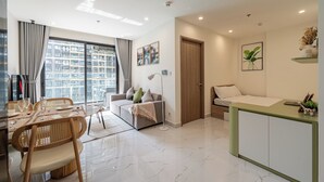 Una sala de estar moderna con un sofá, una mesa de comedor y sillas. Hay un ventanal con cortinas, una puerta y una pequeña cocina con mostrador.