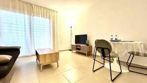 Una sala de estar con sofá, una mesa de centro, televisor, lámpara y una mesa de comedor con sillas.