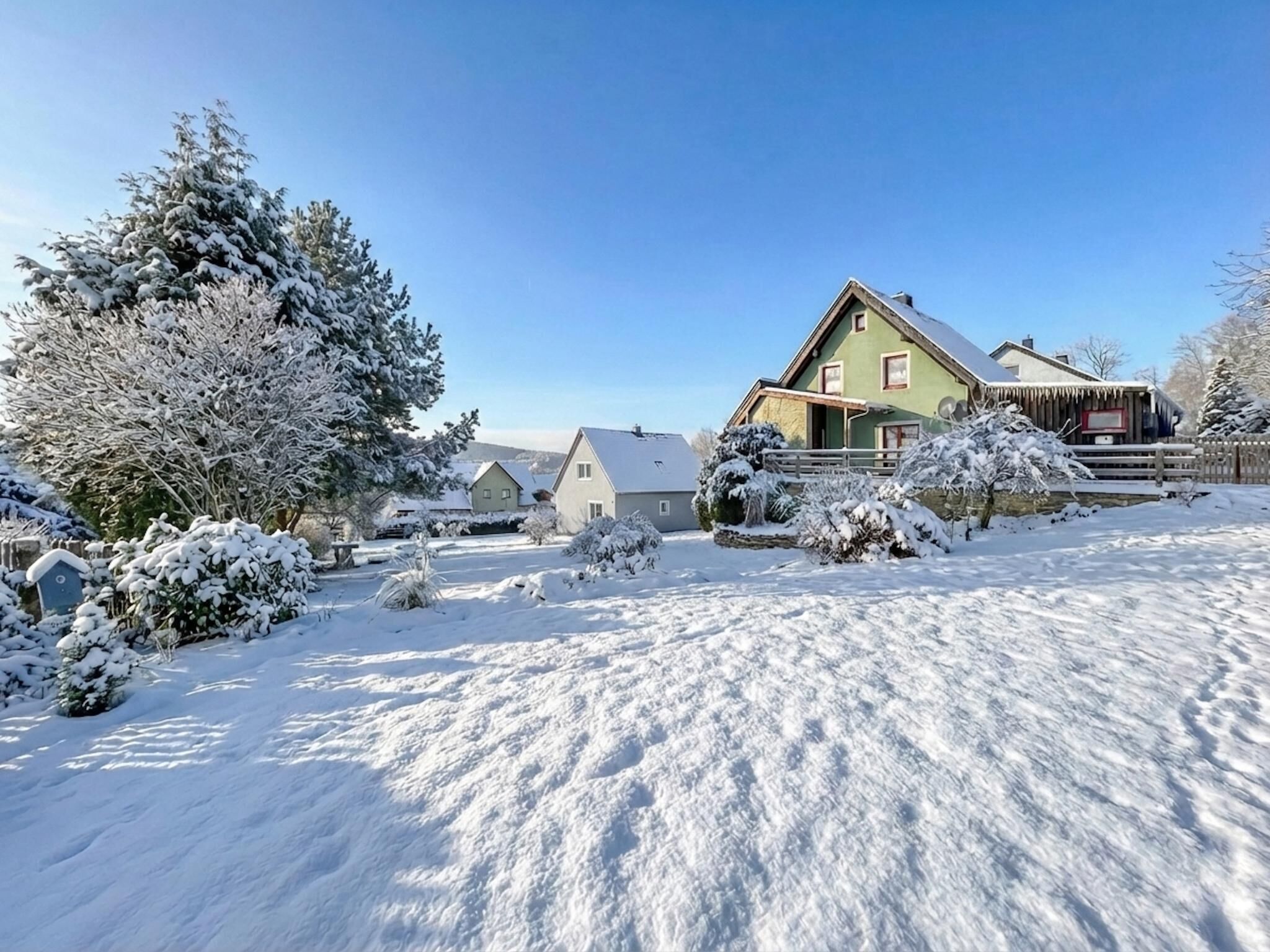 Een besneeuwde woonwijk met huizen, bomen en een heldere lucht.