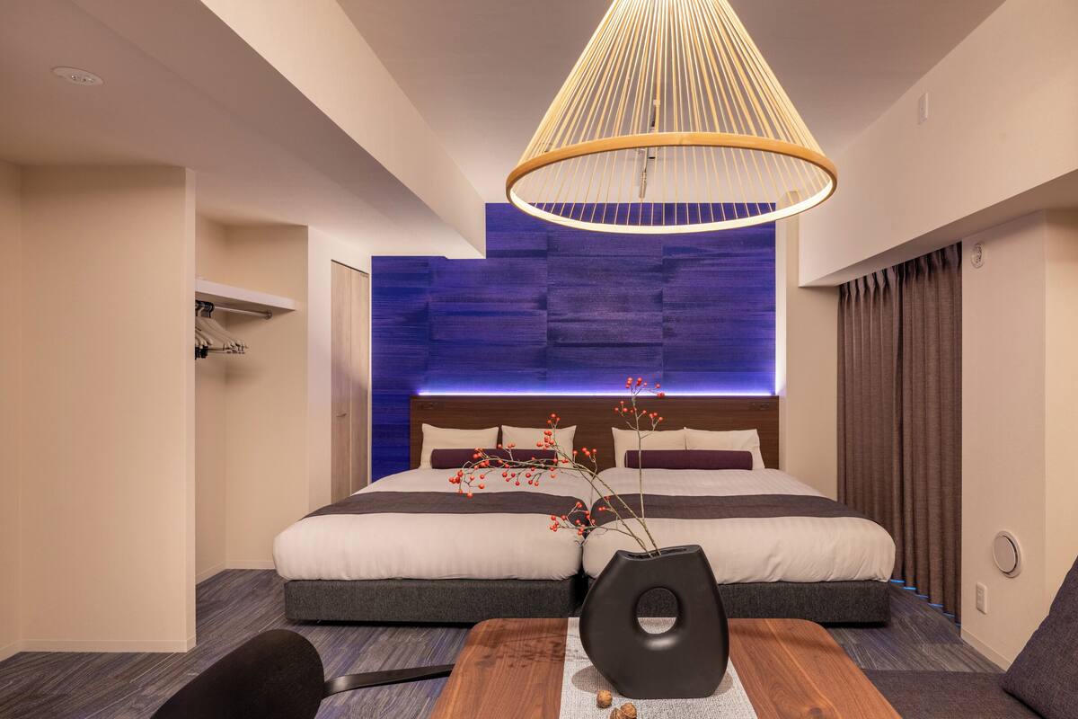 Una habitación de hotel moderna con una cama grande, una mesita de madera, un jarrón con flores rojas y una lámpara colgante.
