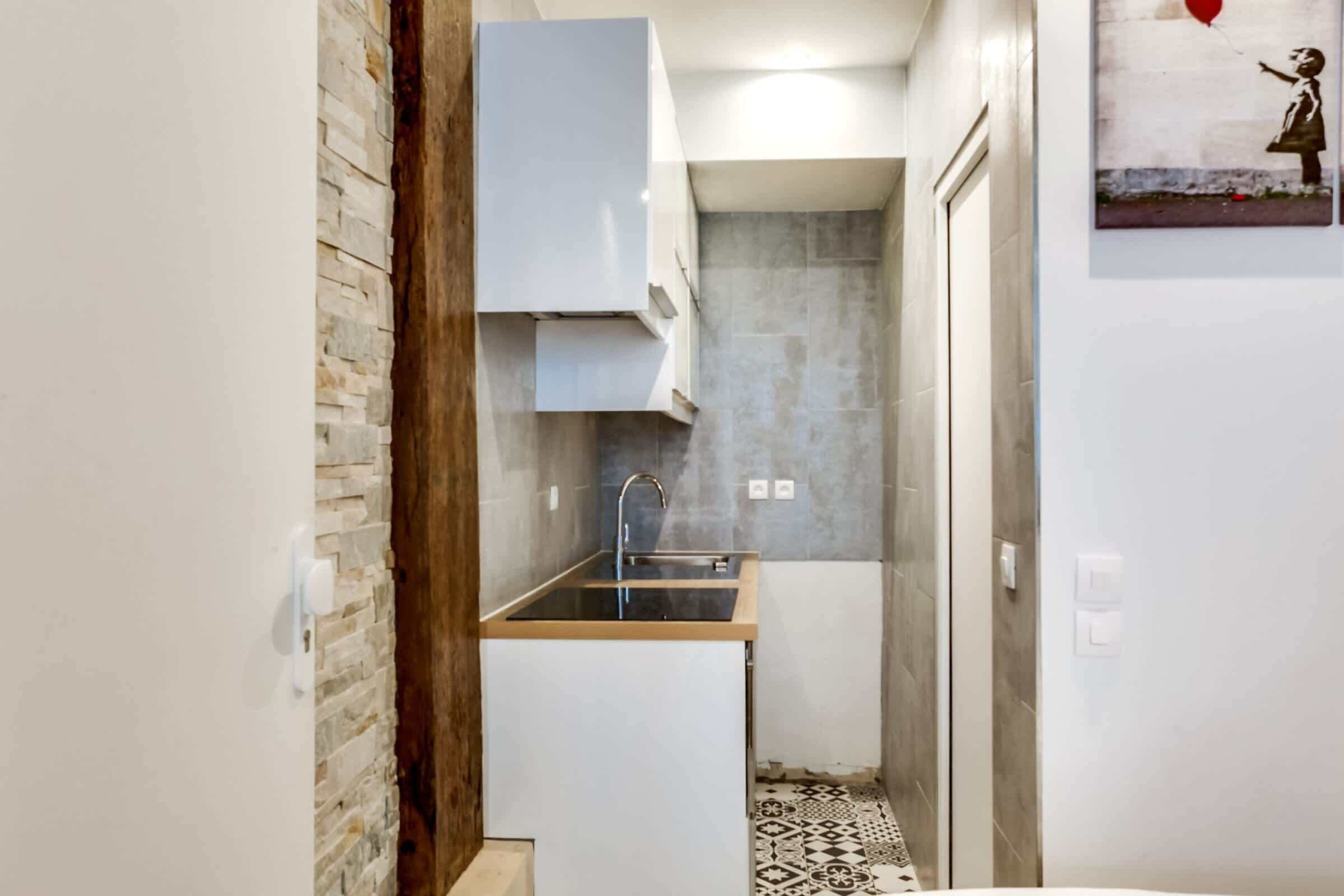 A narrow kitchen with a built-in sink, white cabinets, and a patterned floor.