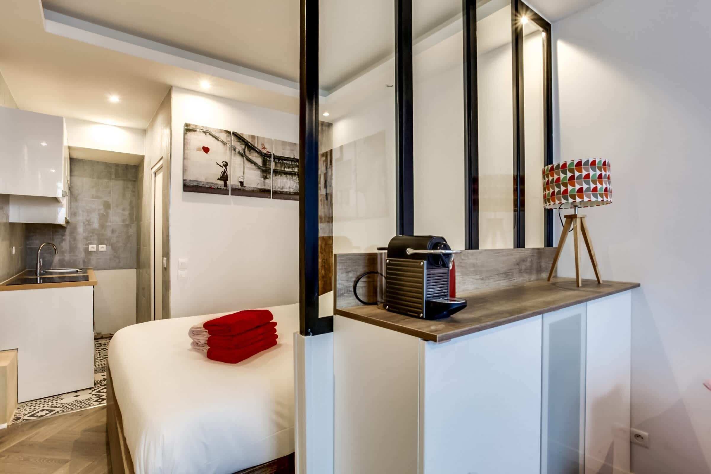 Una habitació d'hotel moderna amb un llit, una cuineta petita, un mirall gran i una làmpada única.