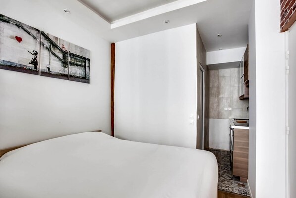 A modern hotel room with a large bed, a small kitchenette, and a bathroom visible through an open door.