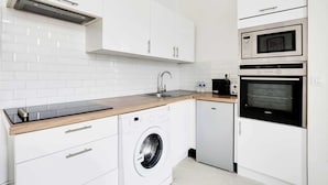 A modern kitchen with white cabinetry, a built-in washing machine, a dishwasher, a microwave, and an oven. - Appartement Cosy à Bastille - 4 guest - Paris 4 (Paris)