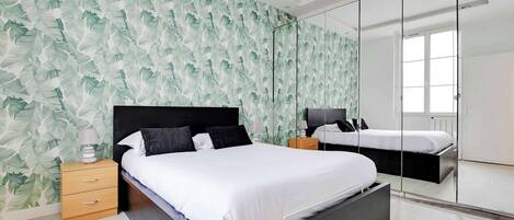 Un dormitorio moderno con una cama grande, una mesita de noche, un aparador, un espejo y una ventana.