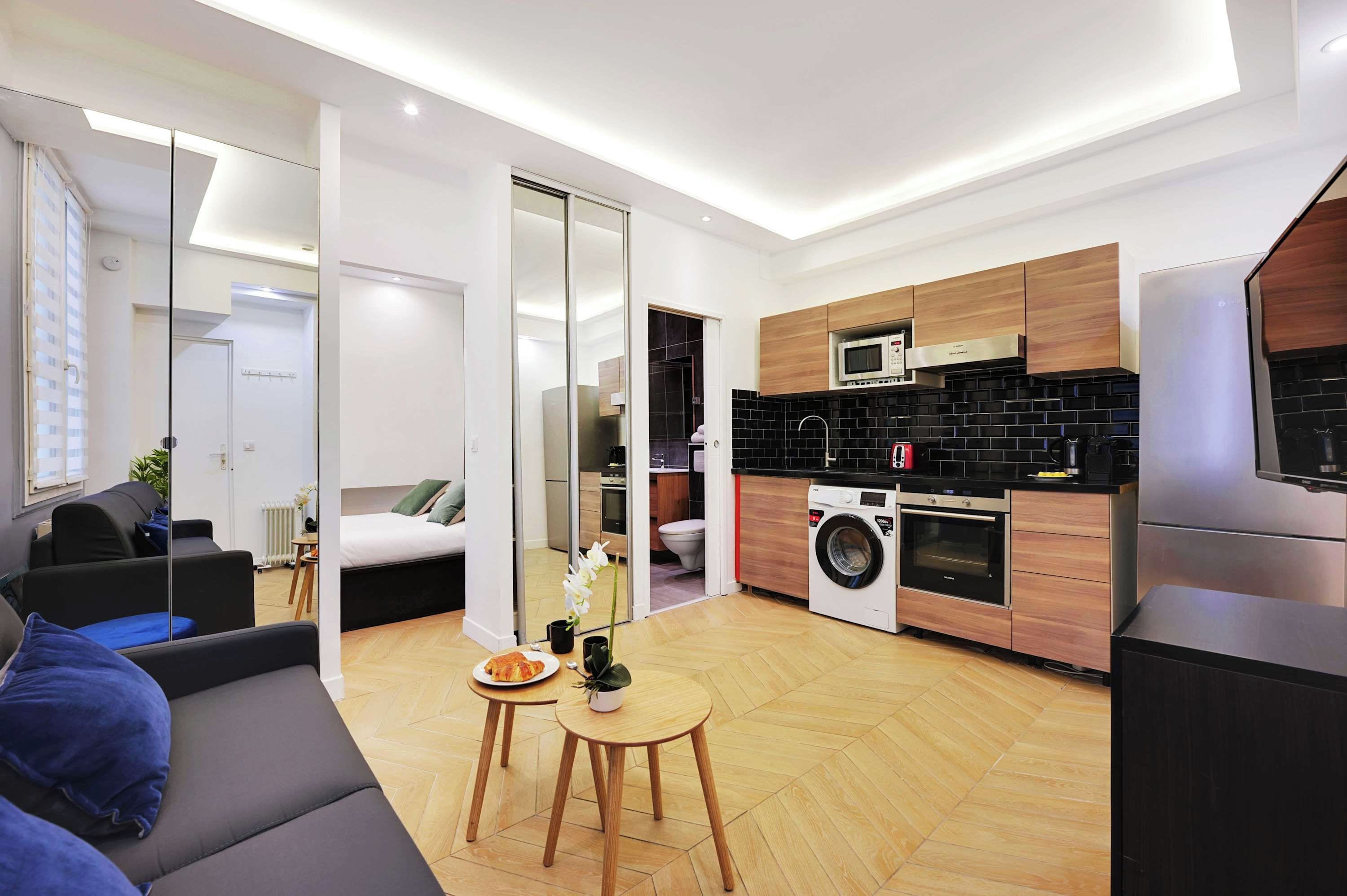 A modern apartment with a kitchen, a living area with a sofa and a small table, and a bedroom with a bed and a sliding door.
