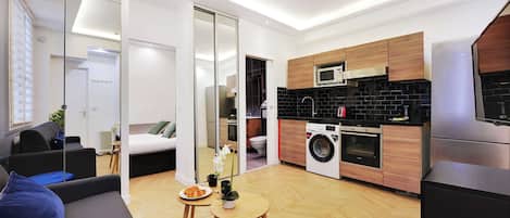 A modern apartment with a kitchen, a living area with a sofa and a small table, and a bedroom with a bed and a sliding door.