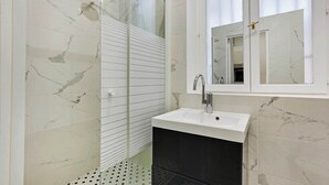 Een moderne badkamer met een douchecabine van glas, een witte wastafel en een grote spiegel erboven.