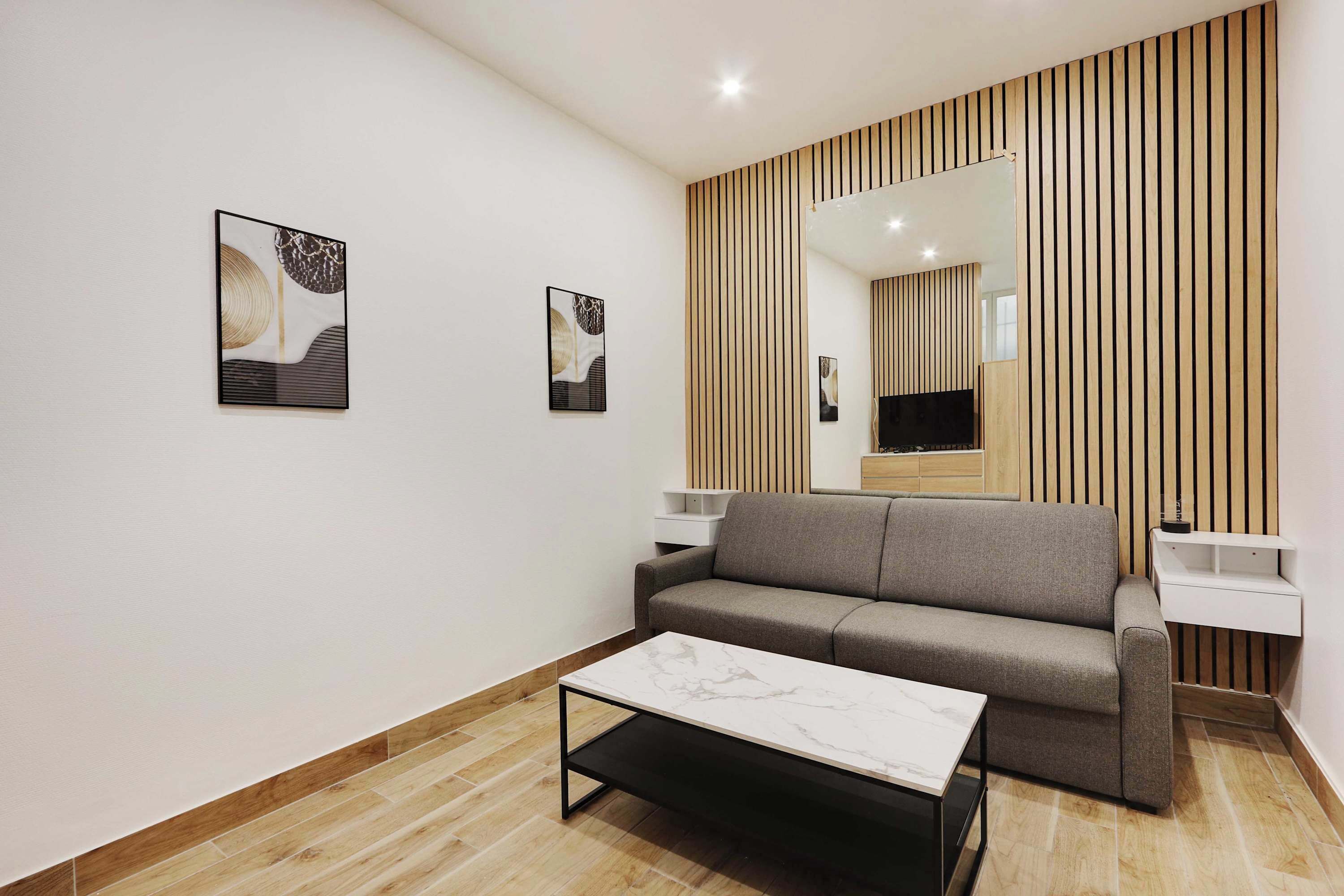 Ein modernes Wohnzimmer mit einem grauen Sofa, einem weißen Couchtisch und zwei an der Wand befestigten Fernsehbildschirmen.