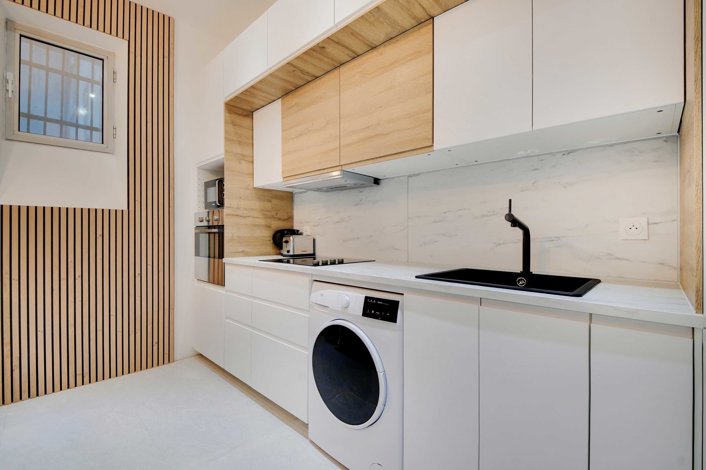 Una cocina moderna con lavadora integrada, microondas y fregadero.