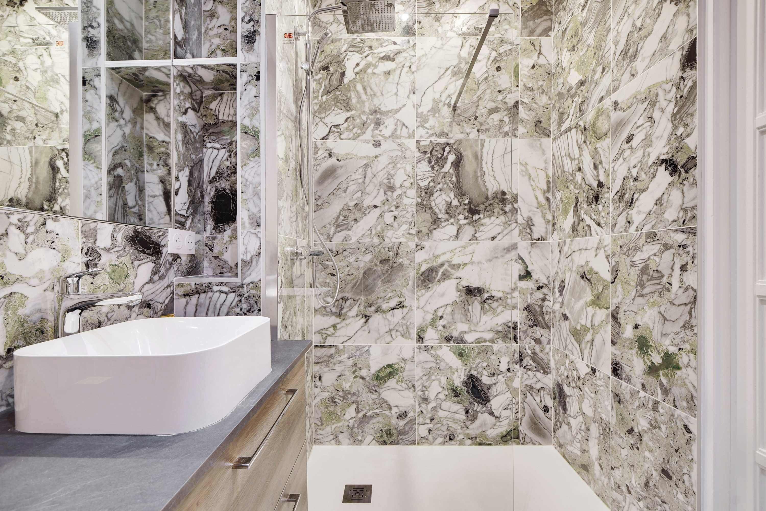 Une salle de bain moderne avec une baignoire sur pieds, une douche à parois de verre et des murs à motifs de marbre.