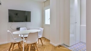 Une pièce moderne avec une table blanche, quatre chaises, un téléviseur à écran plat fixé au mur et une armoire avec une porte.