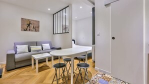 A modern living room with a sofa, a dining table with stools, and a painting on the wall. - Paris 2nd: Studio Near Metro, High-Speed WiFi (Paris)