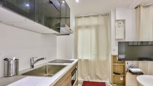A compact kitchen with a double sink, stainless steel faucet, and a modern range hood. - Paris 2nd: Studio Near Metro, High-Speed WiFi (Paris)