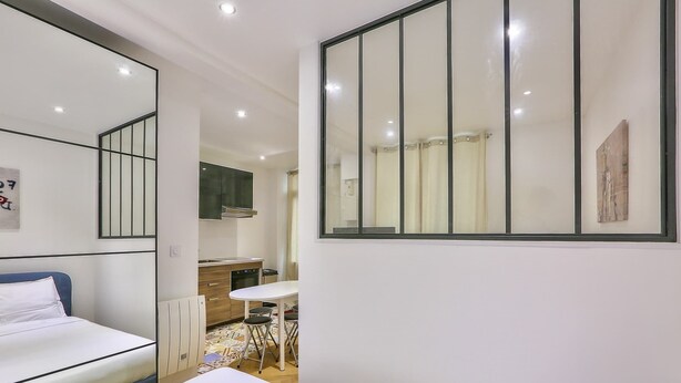A hotel room with a bed, a small kitchenette, a dining table, and a large mirror. - Paris 2nd: Studio Near Metro, High-Speed WiFi (Paris)