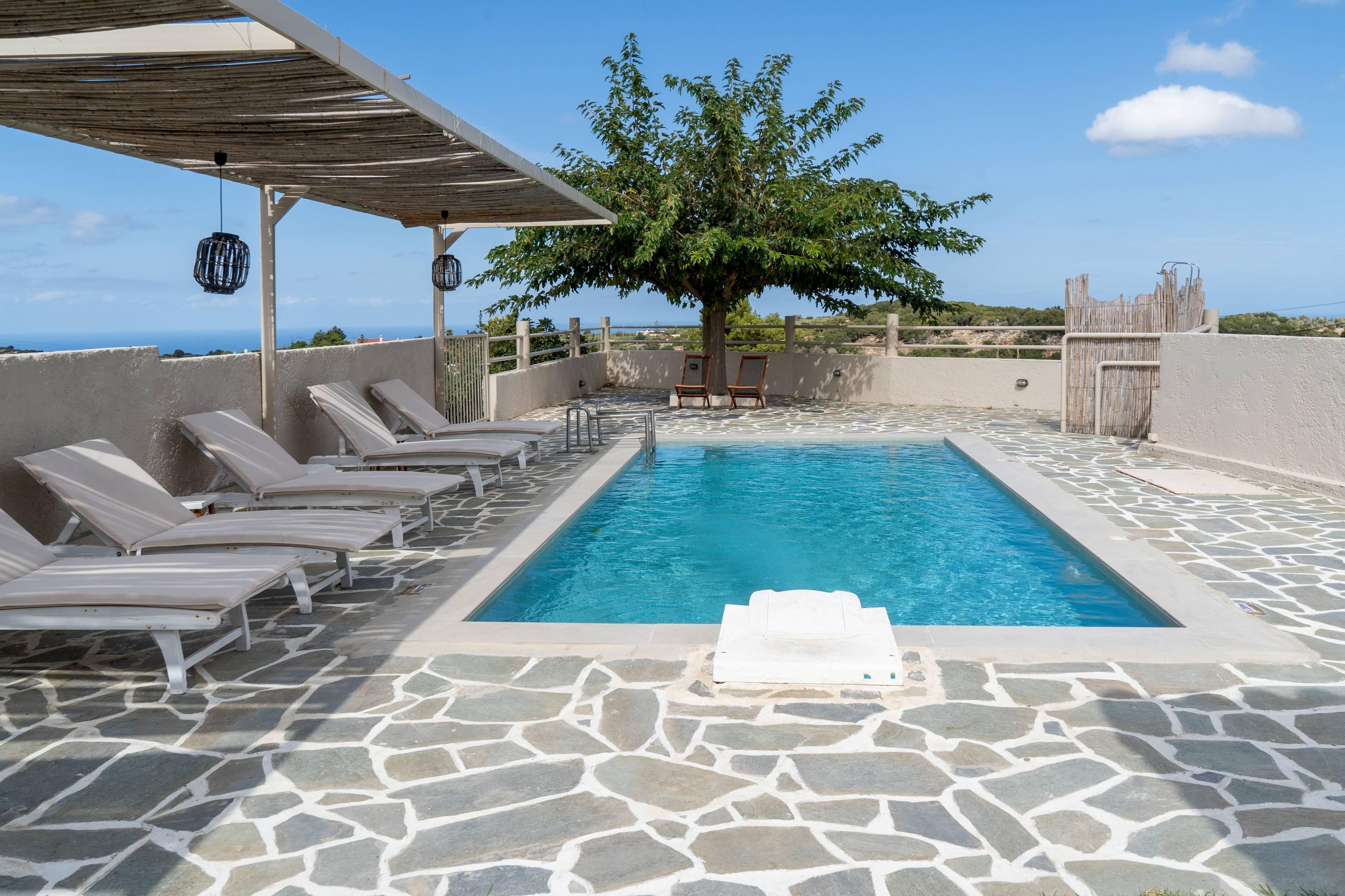 A pool area with lounge chairs, a tree, and a view of the sea.