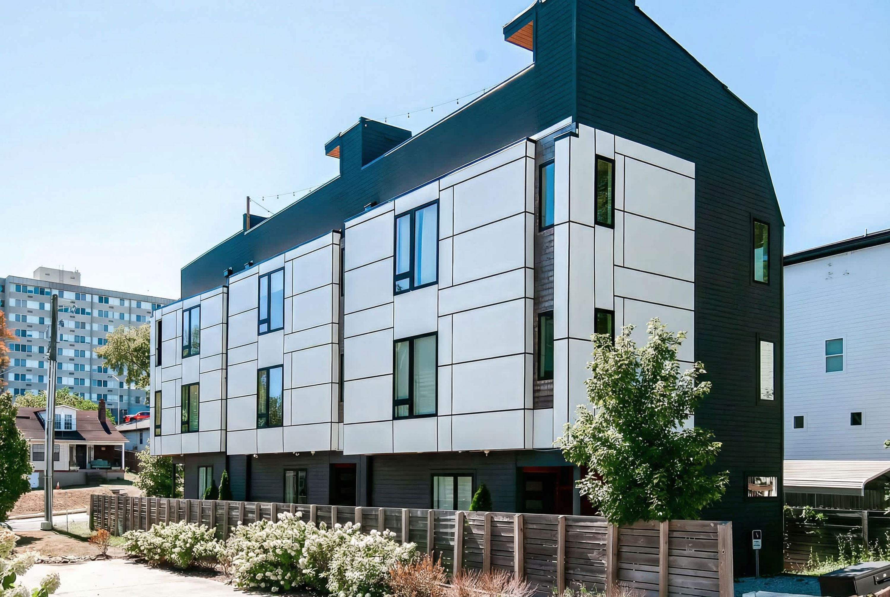 A modern multi-story building with a flat roof, large windows, and a wooden fence in the foreground.