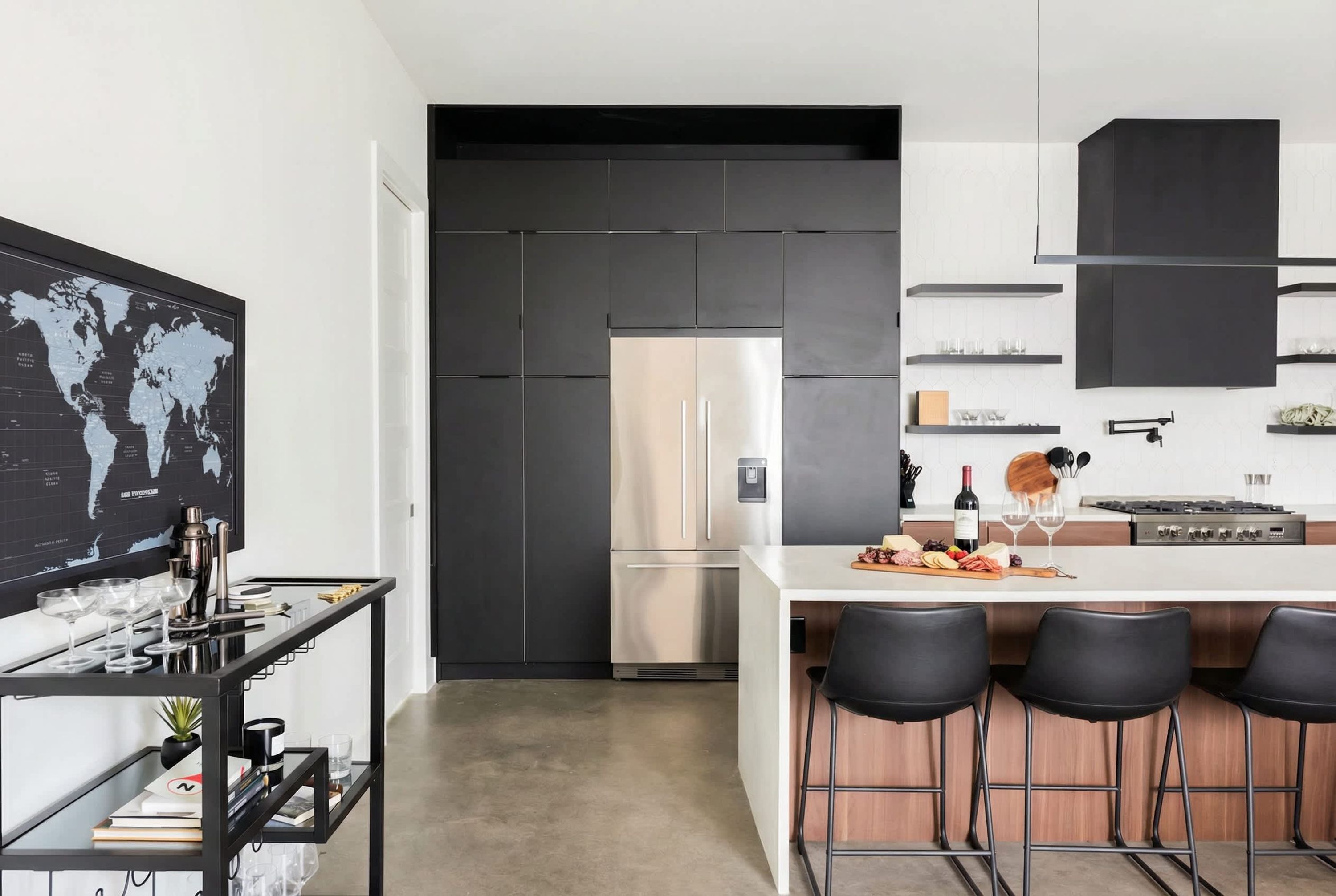 Une cuisine moderne avec un réfrigérateur en acier inoxydable, un plan de travail blanc, des tabourets de bar noirs et une étagère noire fixée au mur.