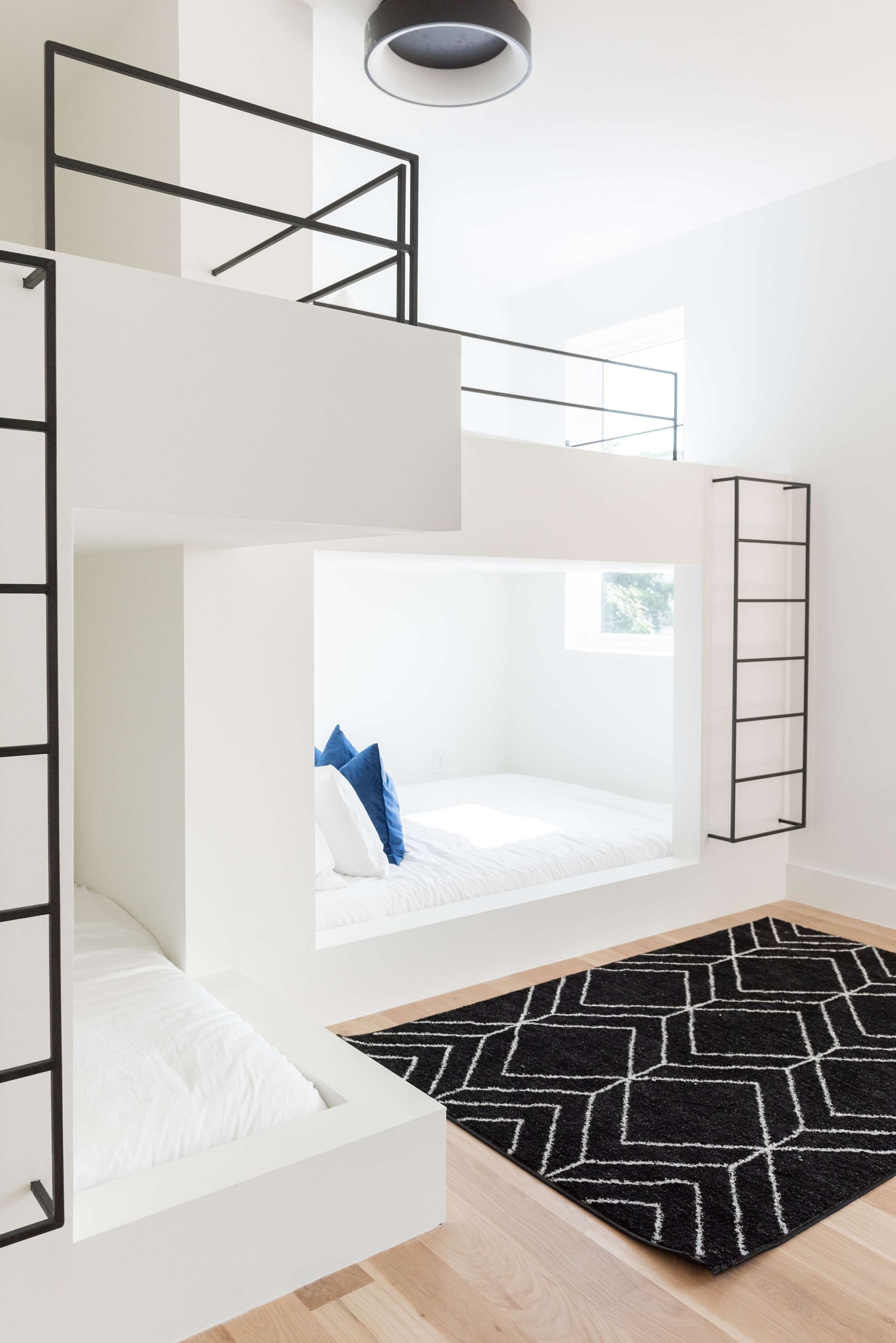 A modern, multi-level bunk bed room with a black and white geometric rug.