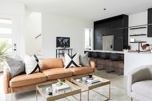 A modern living room with a sofa, coffee table, and a kitchen area with bar stools.