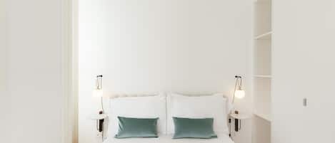 A minimalist bedroom with a large bed, two bedside lamps, and a white wardrobe.