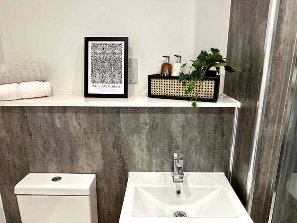 Une salle de bain équipée de toilettes, d’un lavabo, d’œuvres d’art encadrées, d’articles de toilette et d’une plante en pot.