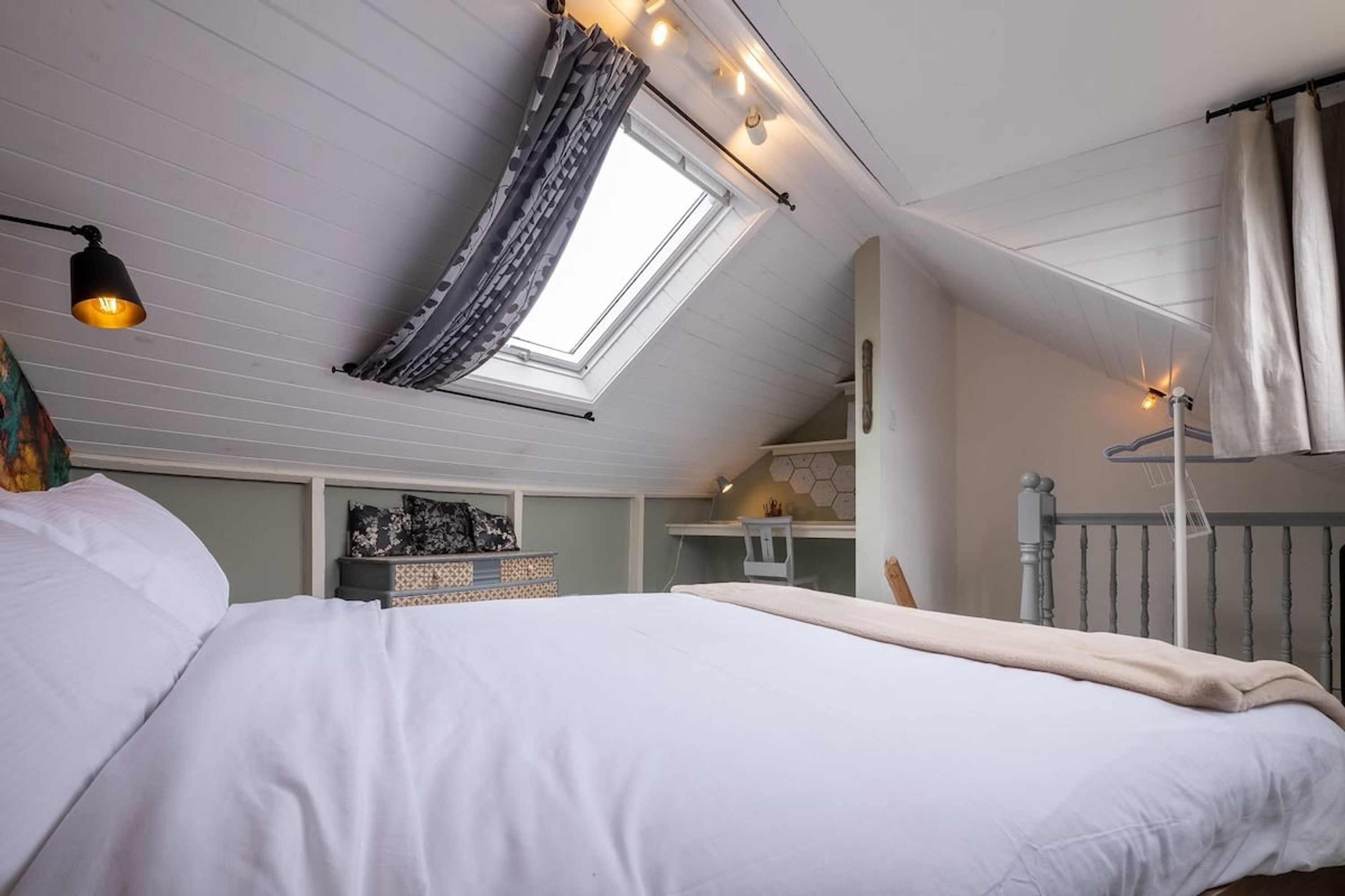 Quarto com clarabóia, cama, escrivaninha e radiador.