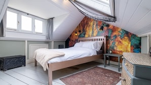 A bedroom with a sloped ceiling, a bed, a small table, a dresser, and a colorful abstract wall. - Host Stay Wakefield Apartment (Brighton)