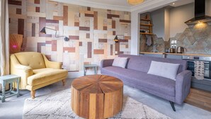 A living room with a sofa, armchair, coffee table, and a kitchen area with a stove and shelves. - Host Stay Wakefield Apartment (Brighton)