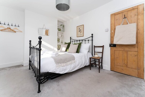A bedroom with a black metal bed frame, white bedding, a wooden door, and a hanging bag.