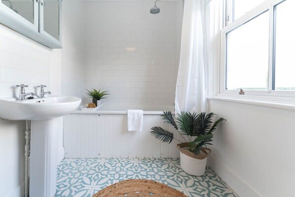 A bathroom with a white sink, a bathtub, and a shower. There is a window with a curtain, and a plant is placed near the window. - Host Stay Centurion House (Brighton)