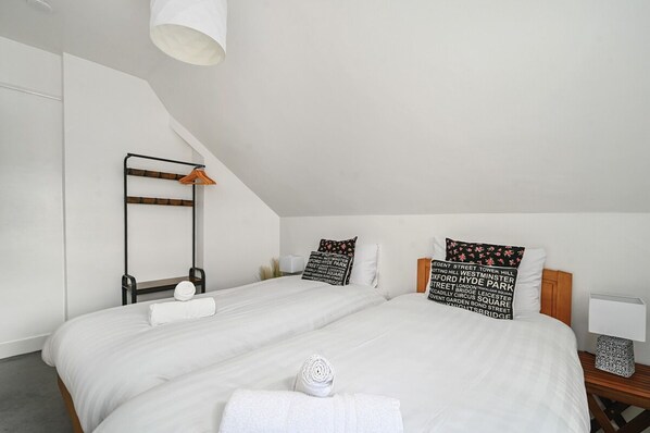 A modern bedroom with a sloped ceiling, two beds, a bedside table, a hanging light fixture, and decorative pillows. - Host Stay The Cliff Greenhouse (Brighton)