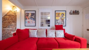 A red sectional sofa with patterned cushions, a wooden coffee table, and two framed movie posters on the wall. - Host Stay George Street Townhouse (Brighton)
