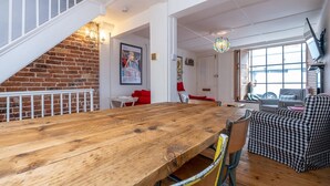 A spacious room with a large wooden table, a checkered sofa, and a staircase with a brick wall. - Host Stay George Street Townhouse (Brighton)