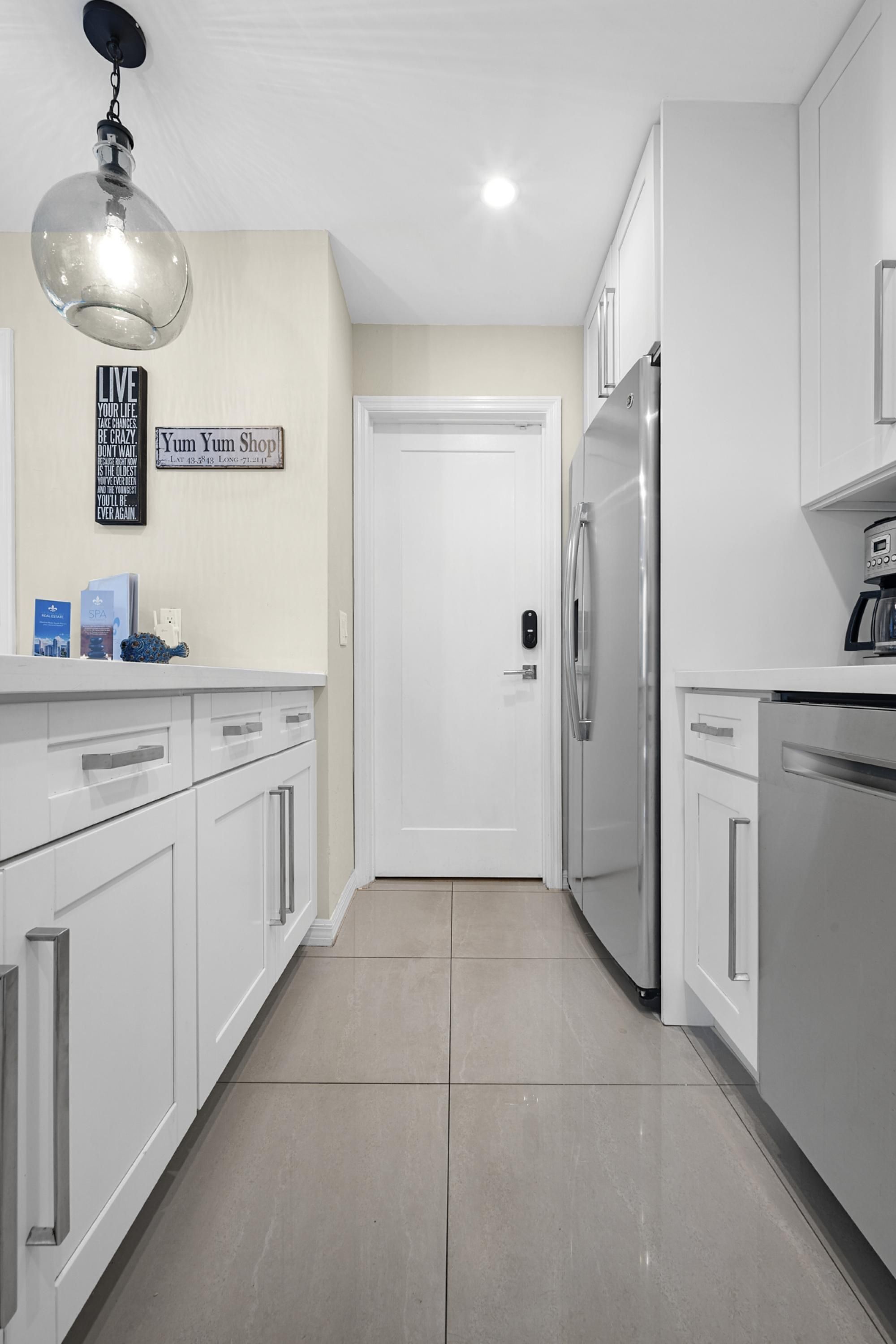 A modern kitchen with white cabinetry, stainless steel appliances, and a tiled floor.